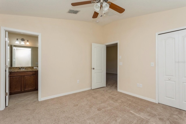 unfurnished bedroom featuring a closet, connected bathroom, light colored carpet, ceiling fan, and sink