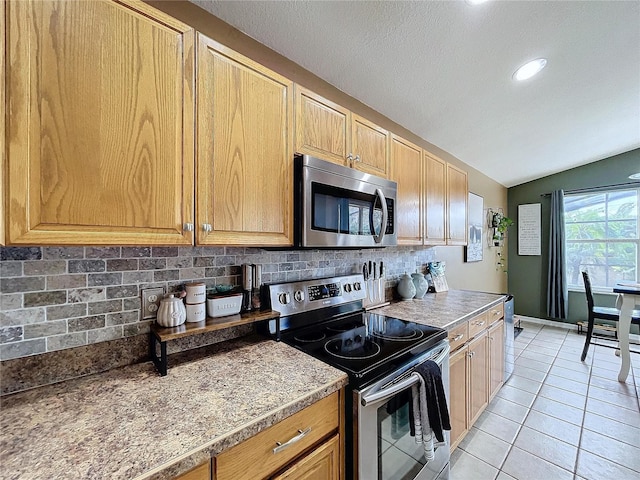 kitchen featuring backsplash, light tile patterned flooring, vaulted ceiling, and appliances with stainless steel finishes