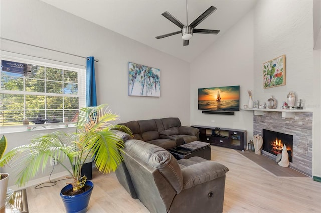 living room featuring ceiling fan, a fireplace, vaulted ceiling, and light hardwood / wood-style flooring