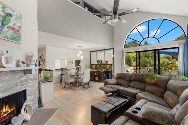 living room with a towering ceiling, light wood-type flooring, a stone fireplace, and ceiling fan