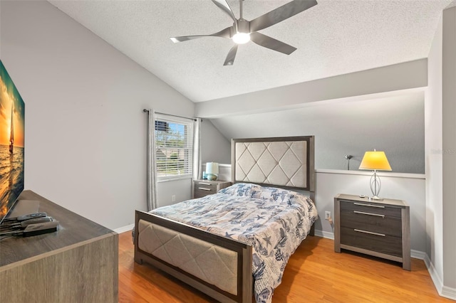 bedroom with a textured ceiling, ceiling fan, light hardwood / wood-style floors, and lofted ceiling