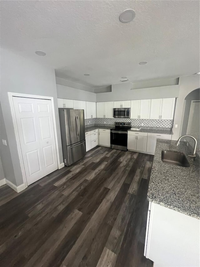 kitchen featuring white cabinetry, sink, light stone counters, appliances with stainless steel finishes, and dark wood-type flooring