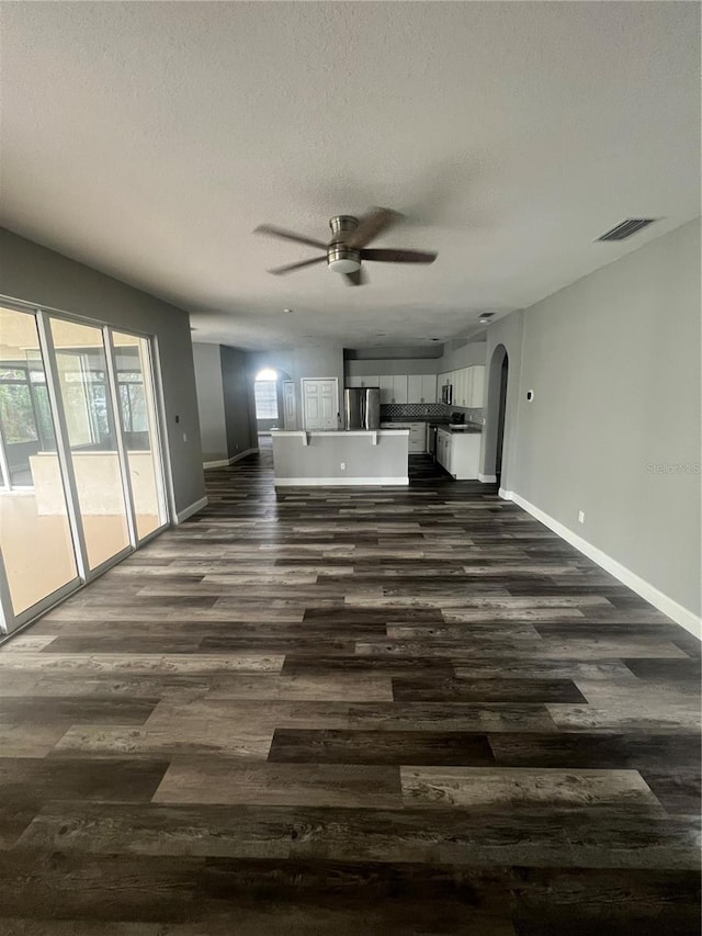 unfurnished living room with dark hardwood / wood-style flooring, a textured ceiling, and ceiling fan