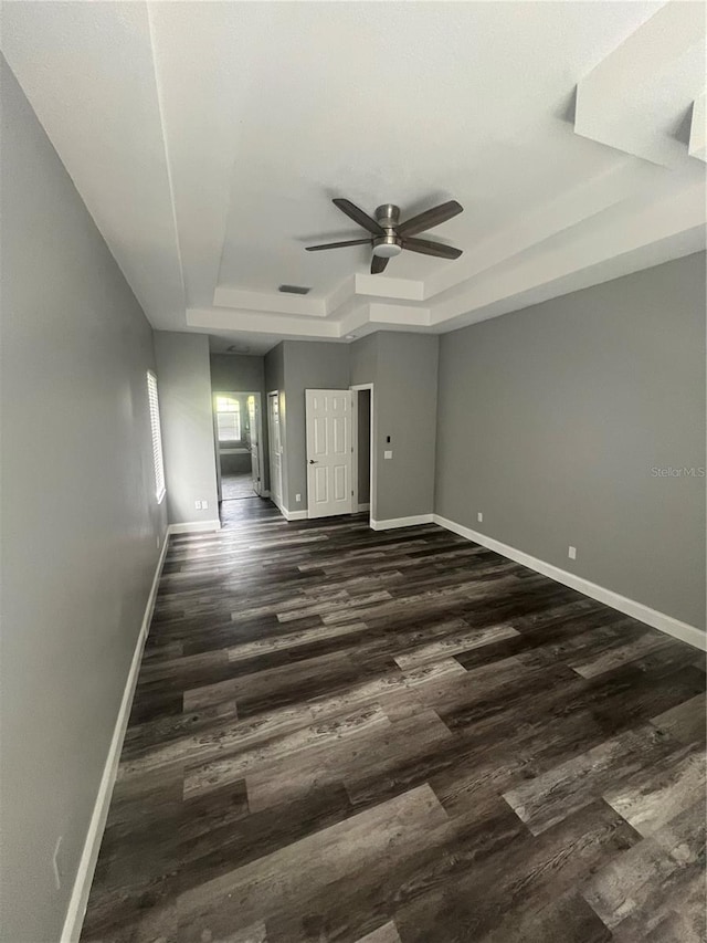 unfurnished room with ceiling fan, dark hardwood / wood-style floors, and a tray ceiling