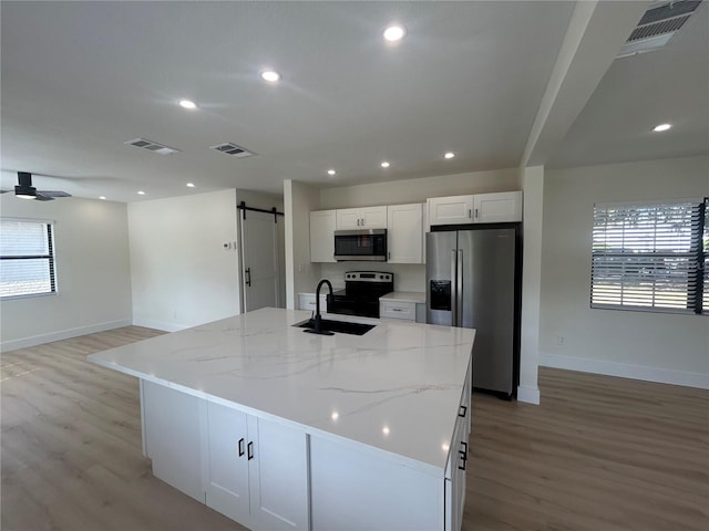 kitchen with white cabinetry, light stone countertops, a barn door, a center island with sink, and appliances with stainless steel finishes