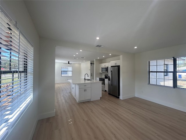 kitchen with white cabinetry, sink, light hardwood / wood-style floors, a center island with sink, and appliances with stainless steel finishes