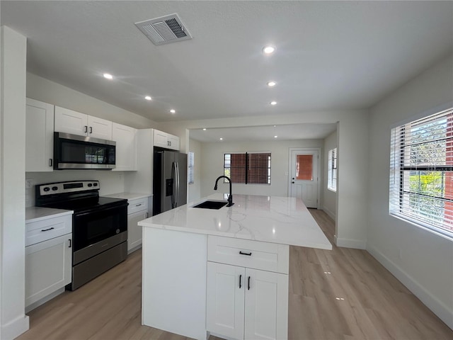 kitchen with a kitchen island with sink, sink, appliances with stainless steel finishes, light stone counters, and white cabinetry