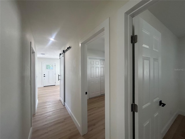 corridor with light wood-type flooring and a barn door