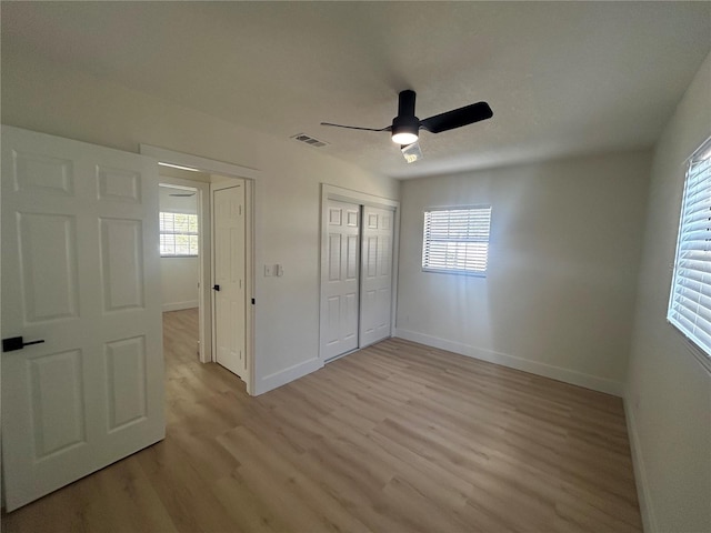 unfurnished bedroom featuring ceiling fan, light wood-type flooring, multiple windows, and a closet