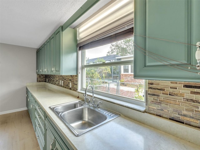 kitchen featuring sink, tasteful backsplash, a textured ceiling, light wood-type flooring, and green cabinets