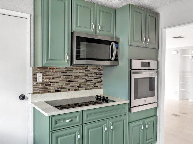 kitchen with appliances with stainless steel finishes, green cabinets, a textured ceiling, and backsplash