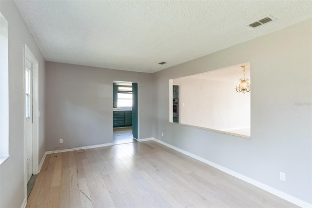 empty room featuring a notable chandelier, a textured ceiling, and light hardwood / wood-style floors