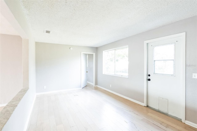 empty room with a textured ceiling and light hardwood / wood-style floors