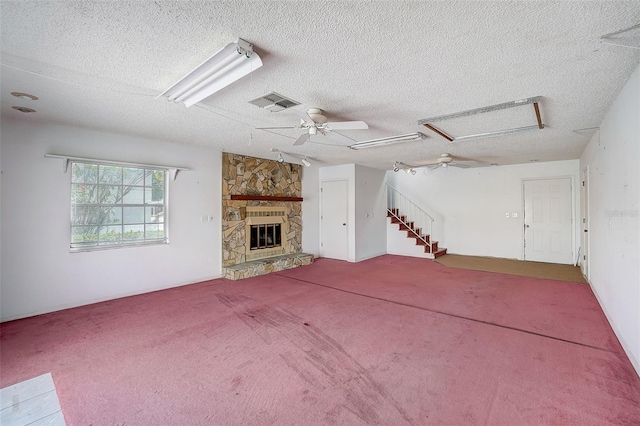 unfurnished living room featuring ceiling fan, a stone fireplace, a textured ceiling, and carpet floors