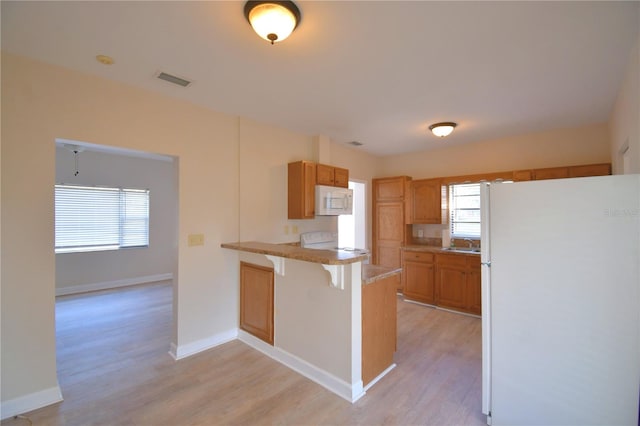 kitchen with a breakfast bar, white appliances, sink, light hardwood / wood-style flooring, and kitchen peninsula