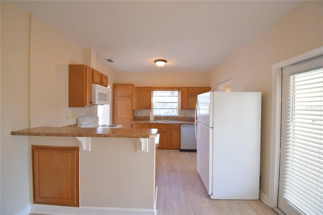 kitchen with kitchen peninsula, a kitchen breakfast bar, light wood-type flooring, white appliances, and sink