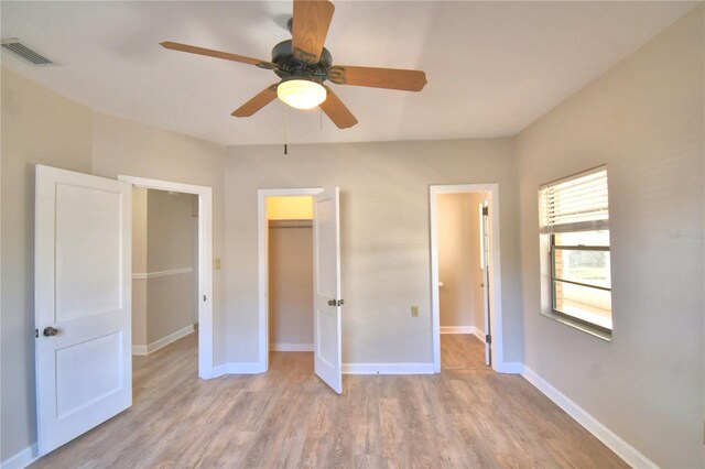 unfurnished bedroom with a walk in closet, ceiling fan, a closet, and light hardwood / wood-style floors