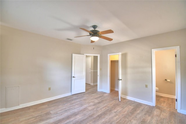 unfurnished bedroom with ensuite bath, ceiling fan, a spacious closet, and light wood-type flooring