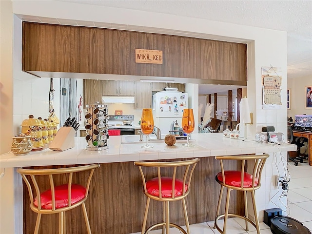 bar with sink, tile patterned floors, range with electric cooktop, white fridge, and tile counters