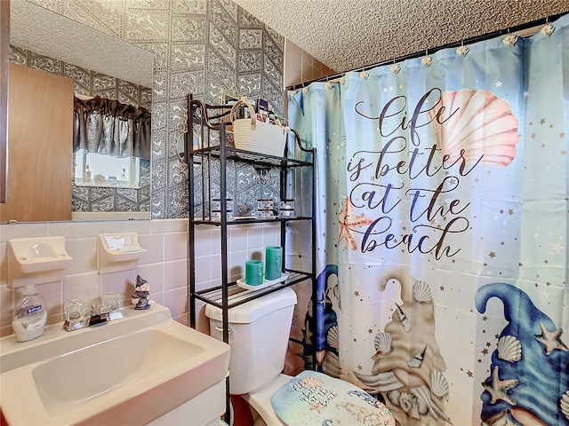 bathroom with sink, walk in shower, a textured ceiling, toilet, and tile walls