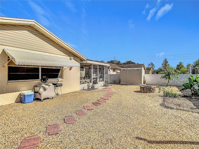 back of property featuring a fire pit, a sunroom, and a storage unit