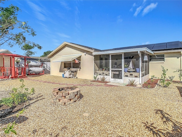 back of property with solar panels, a fire pit, and a sunroom