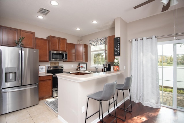 kitchen with light hardwood / wood-style floors, sink, kitchen peninsula, appliances with stainless steel finishes, and a kitchen breakfast bar