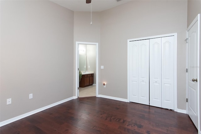 unfurnished bedroom with dark wood-type flooring, a closet, ceiling fan, and a high ceiling