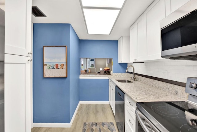 kitchen featuring stainless steel appliances, white cabinetry, sink, tasteful backsplash, and light wood-type flooring