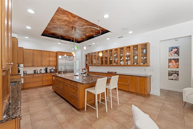 kitchen with a kitchen bar, a center island with sink, appliances with stainless steel finishes, and a tray ceiling