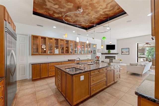 kitchen featuring an island with sink, stainless steel built in fridge, a raised ceiling, and pendant lighting