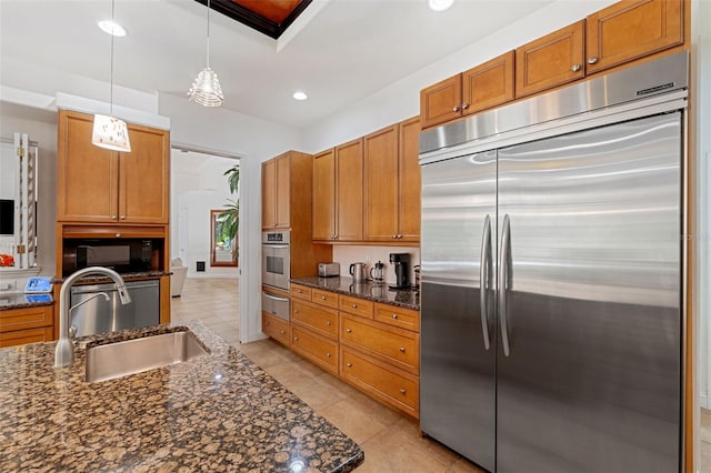 kitchen featuring stainless steel appliances, sink, decorative light fixtures, and dark stone countertops