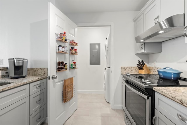 kitchen featuring electric panel, light stone counters, stainless steel range with electric stovetop, light tile patterned flooring, and washer and dryer