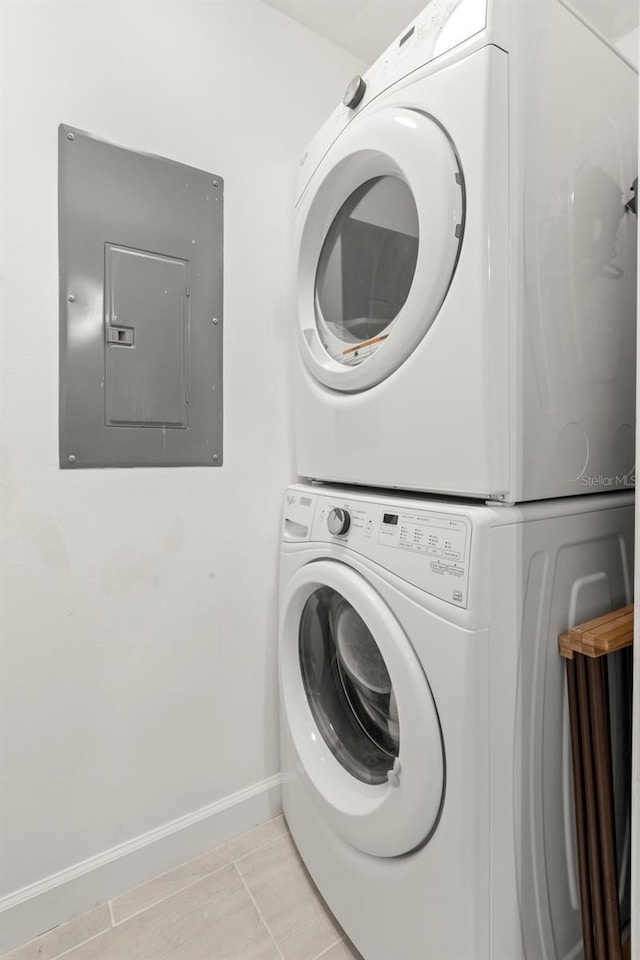 laundry room featuring stacked washer / dryer, electric panel, and light tile patterned flooring