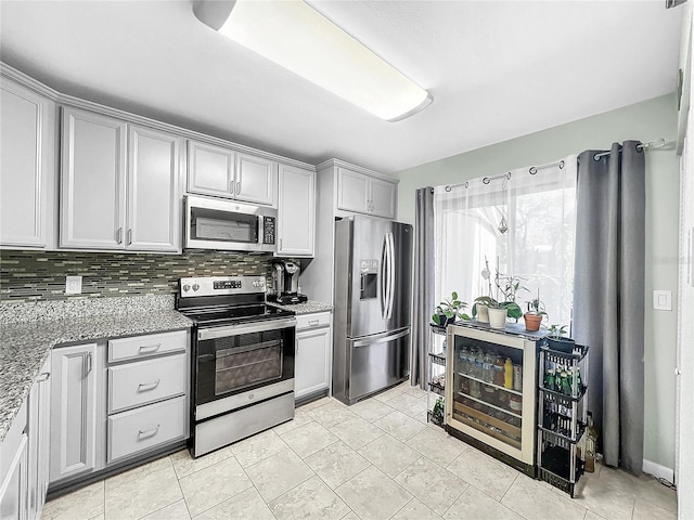 kitchen featuring wine cooler, light stone counters, appliances with stainless steel finishes, gray cabinetry, and decorative backsplash