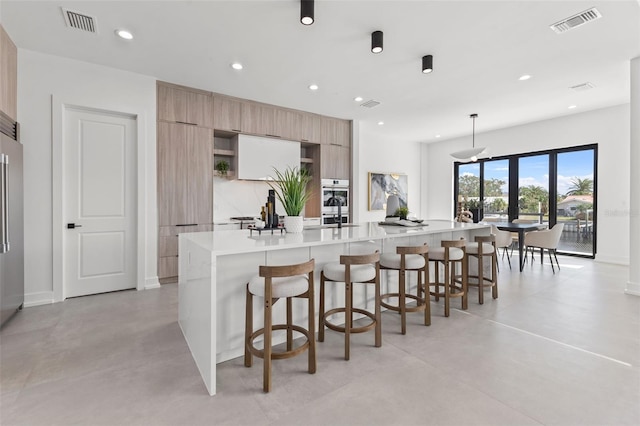 kitchen with a spacious island, a breakfast bar, high quality fridge, and decorative light fixtures