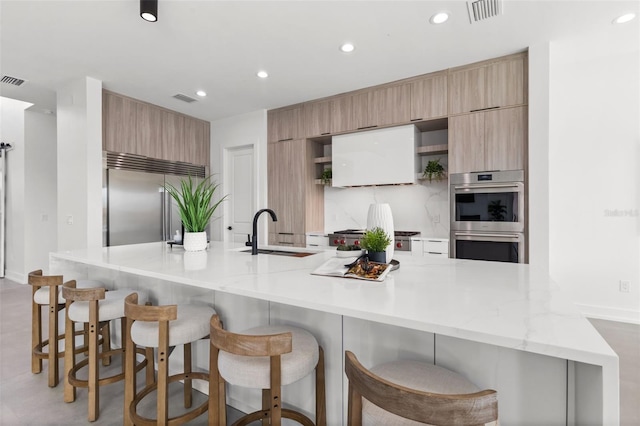 kitchen with sink, a breakfast bar area, stainless steel appliances, light stone counters, and a large island with sink