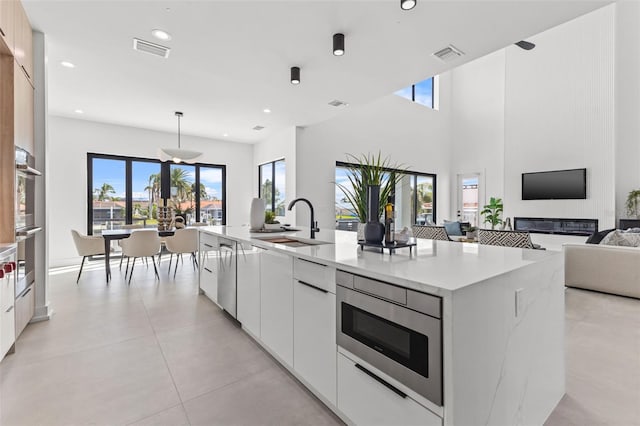 kitchen featuring a kitchen island with sink, hanging light fixtures, sink, and white cabinets