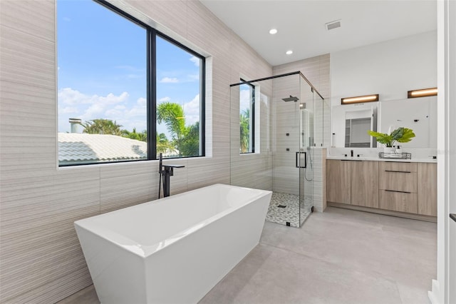 bathroom featuring vanity, concrete flooring, independent shower and bath, and tile walls