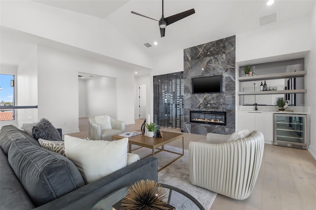 living room featuring vaulted ceiling, light wood-type flooring, beverage cooler, ceiling fan, and a premium fireplace