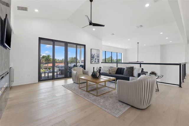 living room with a high ceiling, ceiling fan, and light wood-type flooring