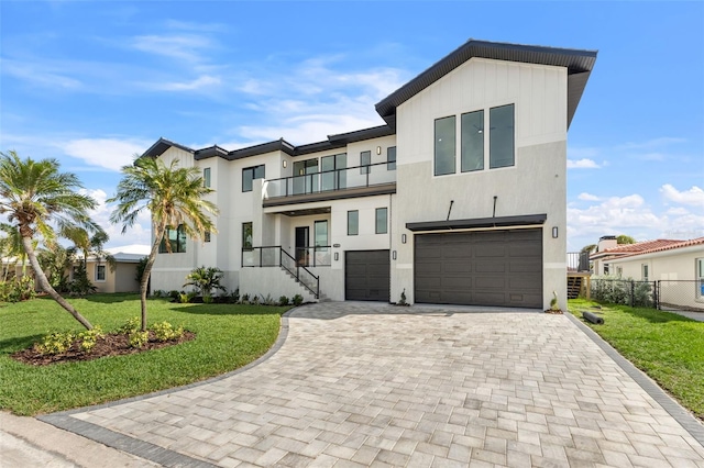 view of front of home featuring a front yard, a balcony, fence, a garage, and decorative driveway