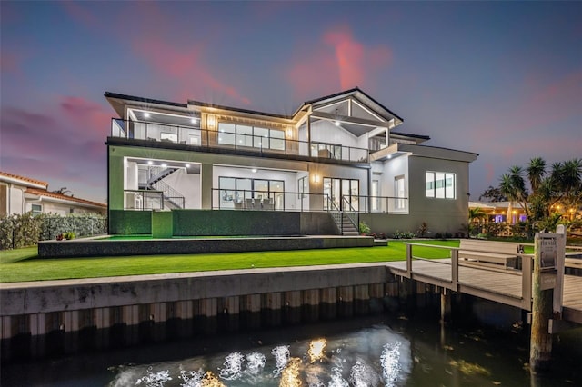 rear view of property with a water view, stairway, stucco siding, a lawn, and a balcony