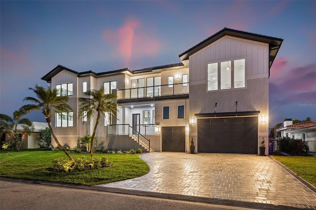 view of front of house with decorative driveway, a front lawn, a balcony, and an attached garage