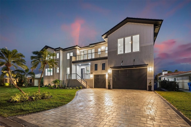 view of front facade featuring a balcony, a yard, stucco siding, a garage, and decorative driveway