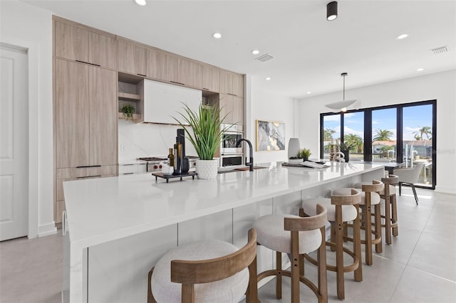 kitchen featuring a spacious island, visible vents, light brown cabinets, a breakfast bar, and modern cabinets