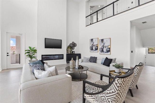 living room with a glass covered fireplace, a high ceiling, and visible vents