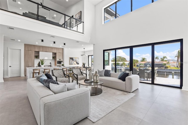 living area featuring visible vents, a water view, concrete flooring, recessed lighting, and a towering ceiling