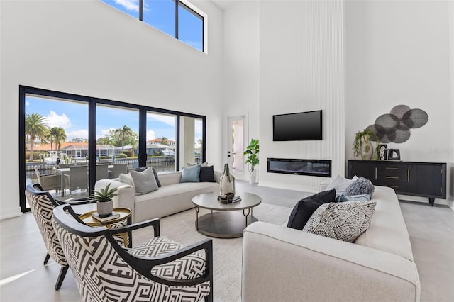 living room with baseboards, a high ceiling, concrete floors, and a glass covered fireplace