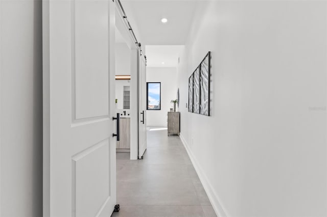 corridor featuring a barn door, recessed lighting, baseboards, and finished concrete floors